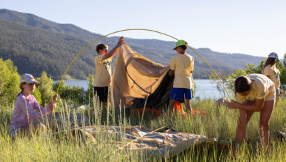 Group of students setting up tents in grasses by a lake.