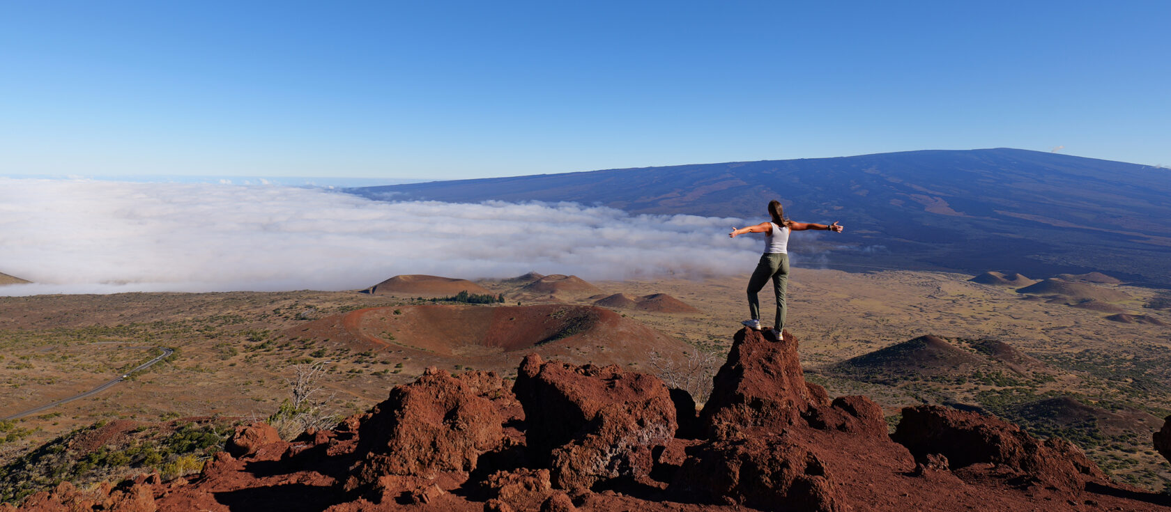 Person with their arms out on the summit of Mauna Kea.
