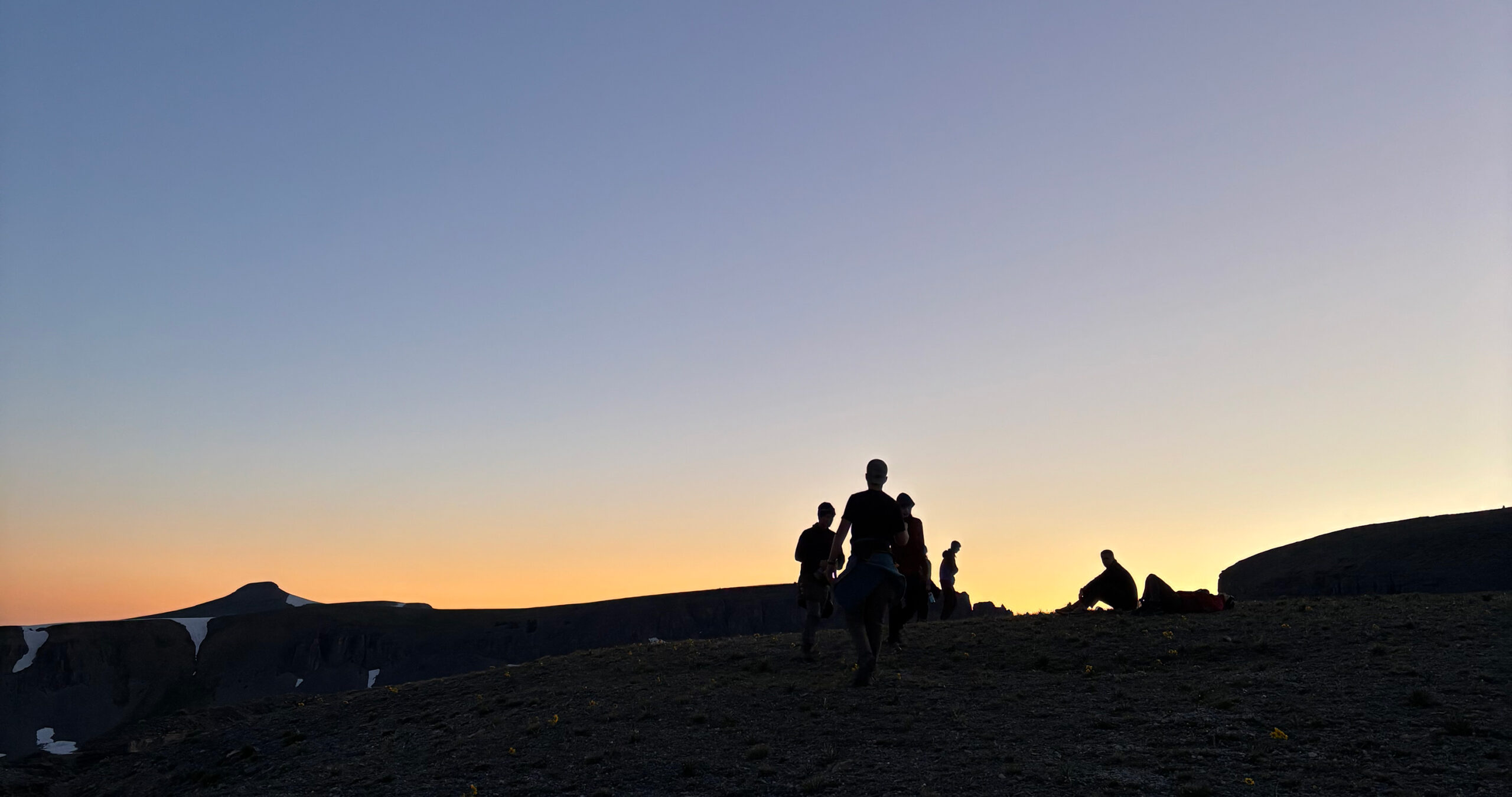 Group of campers walking into the sunset on a mountain pass.