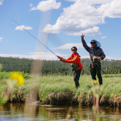 A middle school boy fly fishing with the encouragement of a guide on the shore of a river in Yellowstone National Park.