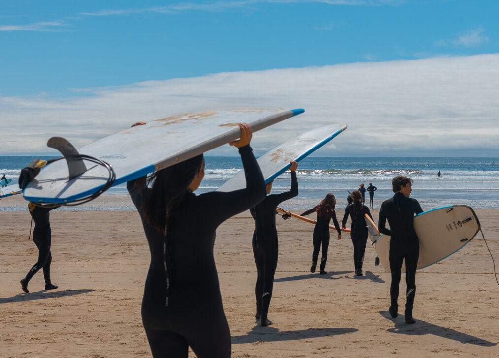 Middle schoolers entering the ocean on the Olympic Coast with surfboards.