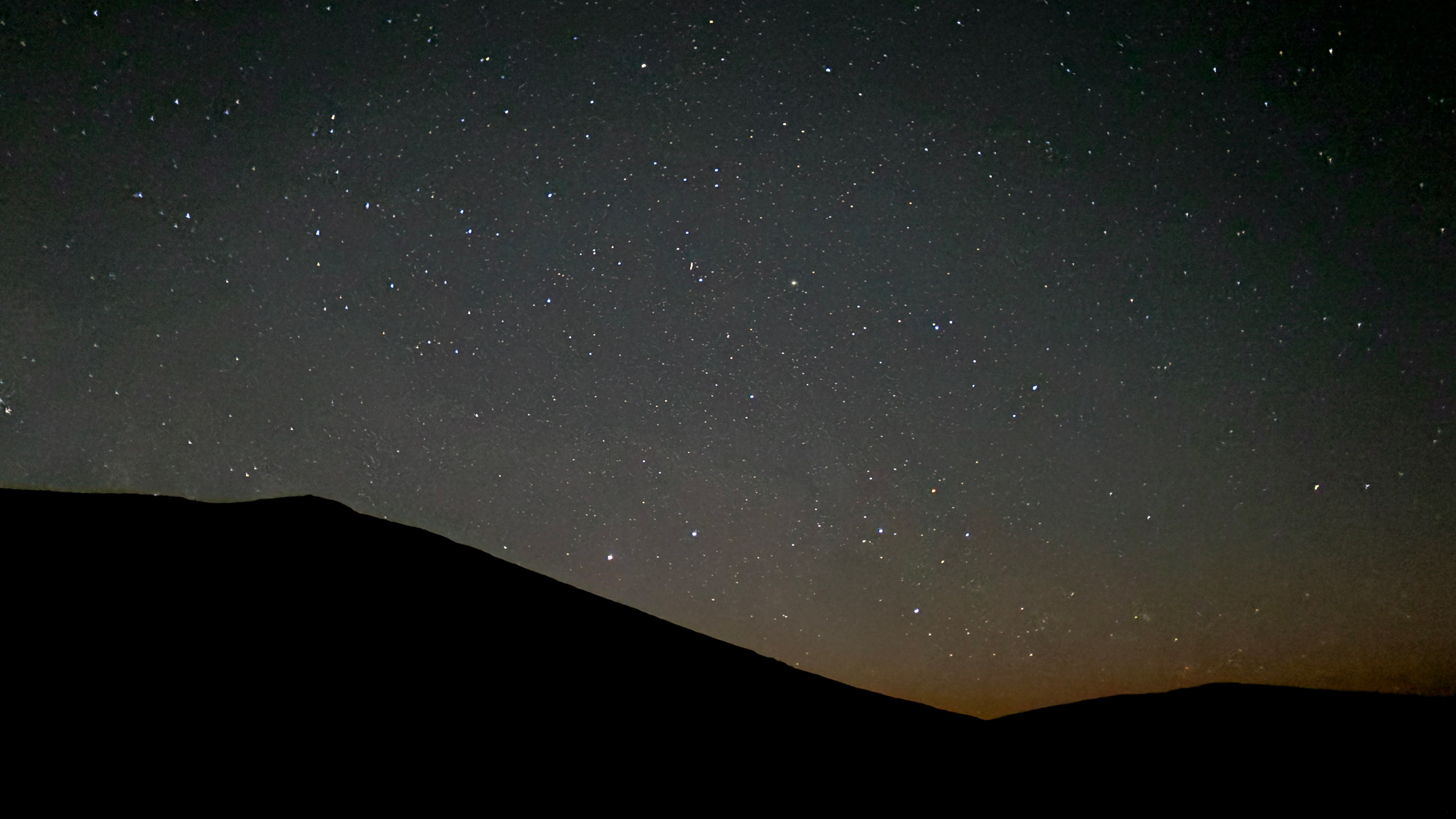 a star filled Wyoming sky with a bit of orange and blue over the mountains.
