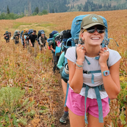 Girl smiling wearing a Teton Valley Ranch Camp hat while backpacking in Wyoming.