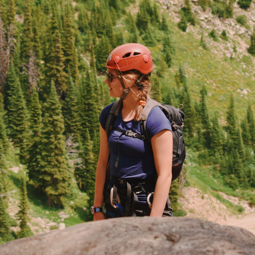Woman wearing a climbing helmet and backpacking looking off into the distance in the Tetons in the summer.