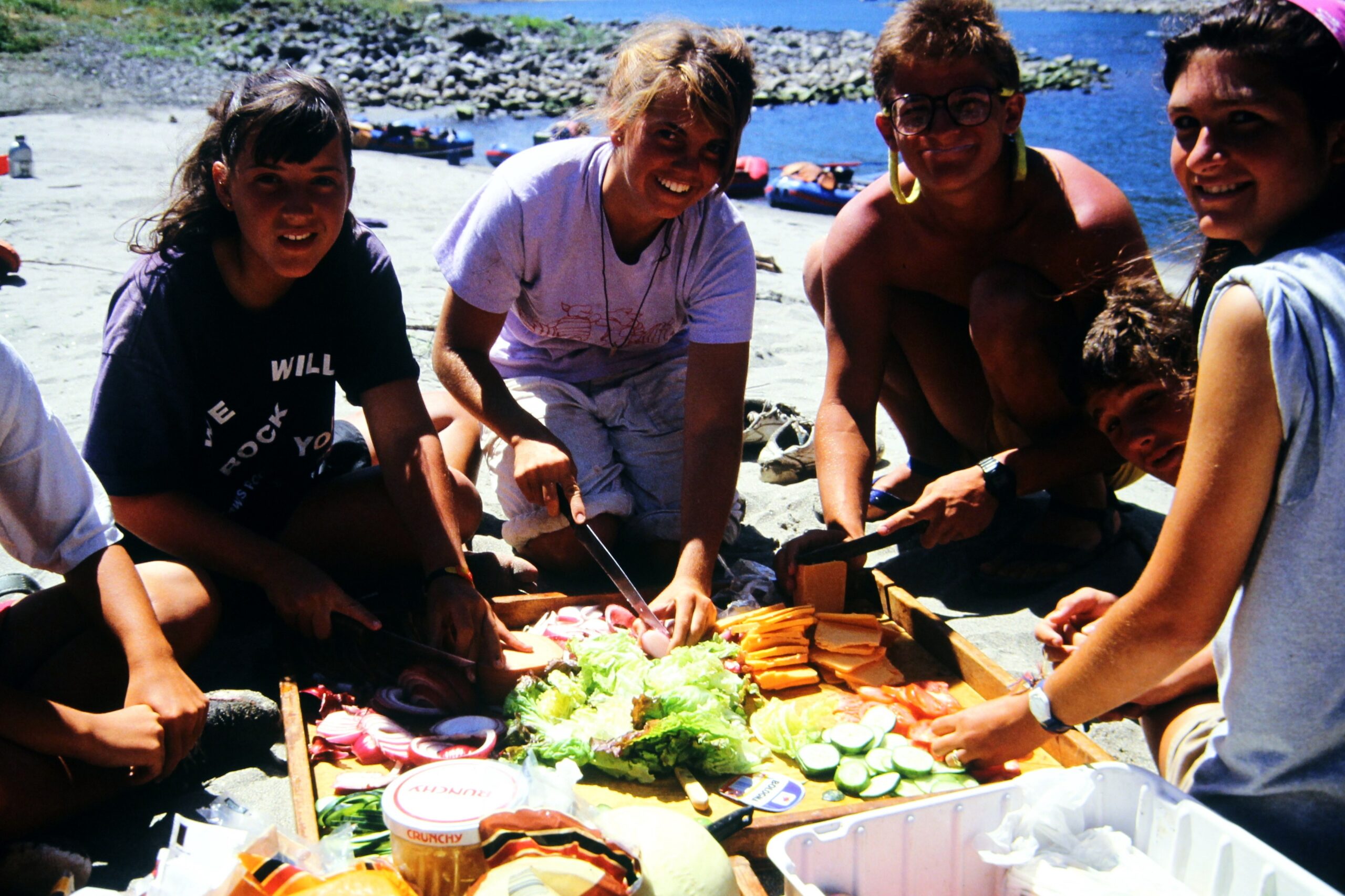 A group of teens in the 1980s cooking together while camping. 